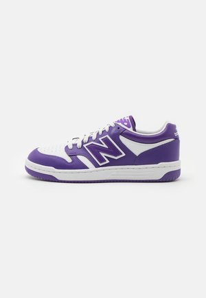 Niskie sportowe buty typu sneaker z białymi i fioletowymi skórzanymi panelami, białymi sznurowadłami i dużym fioletowym logo "N" z boku.