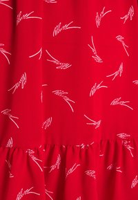 Tissu rouge avec des motifs abstraits blancs en lignes ; la taille froncée ajoute de la texture. Matière lisse et légère.