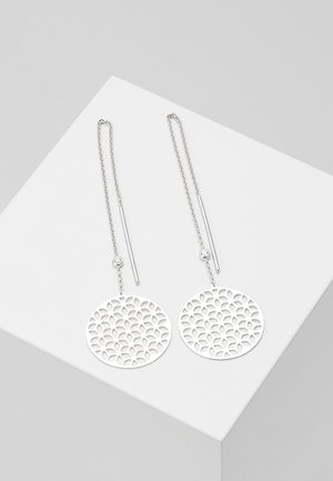 Longues boucles d'oreilles à chaîne argentée avec pendentifs ronds en filigrane présentant un motif floral répété, exposées sur une surface blanche.