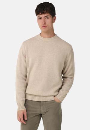 Beige crewneck sweater lavet af blødt materiale; har ribbede manchetter og kant for tekstur. Kombineret med olivengrønne kordfløjspants.
