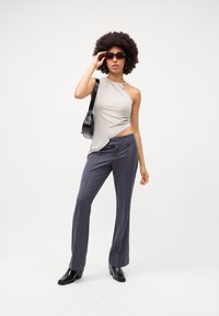 Top beige asimmetrico con dettaglio cut-out, abbinato a pantaloni neri scuri e stivali neri con tacco. Gli accessori includono occhiali da sole neri.
