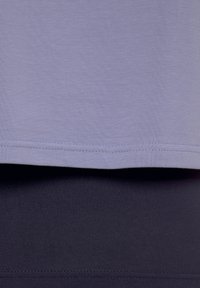 Hellpurpurnes Baumwollmischgewebe-Oberteil, das über einer dunkelblauen Unterlage liegt. Beide haben eine glatte Textur und weisen saubere Säume ohne Verzierungen auf.