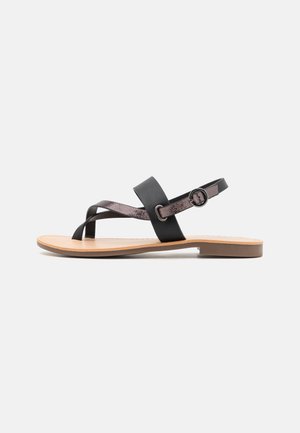 Flad sandal med tanfarvet sål, sort tåloop, krydsende metallisk brun rem, bred sort rem og justerbar ankelspænde.