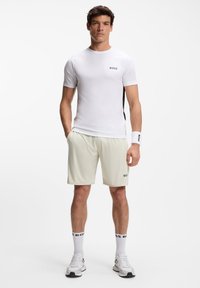 Fehér atlétatrikó fekete oldalsó díszítéssel, világos bézs rövidnadrág, valamint fehér zokni fekete márkajelzéssel; semleges tónusú sportcipőkkel párosítva.