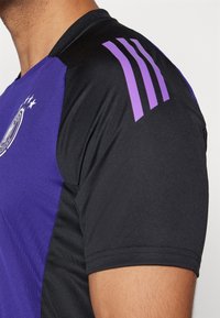 Lila och svart sporttröja med korta ärmar, som har en rund halsringning, subtil textur och tre vertikala lila ränder på axeln.