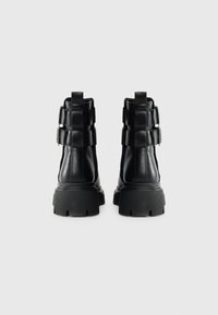 Black leather ankle boots with a chunky sole, featuring buckle accents and a smooth texture. The back shows a structured design.