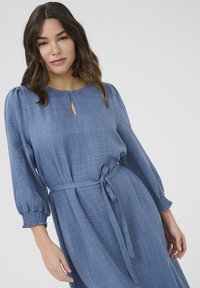 Robe en lin bleu avec de longues manches bouffantes, décolleté en forme de trou de serrure, taille cintrée et ceinture nouée, dotée d'un tissu texturé.