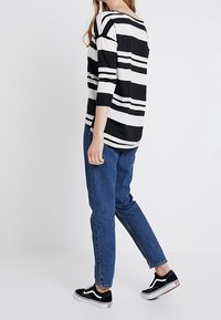 Černobíle pruhovaný top s širokým výstřihem a tříčtvrtečními rukávy, v kombinaci s modrými džíny a černými teniskami s bílou podrážkou.