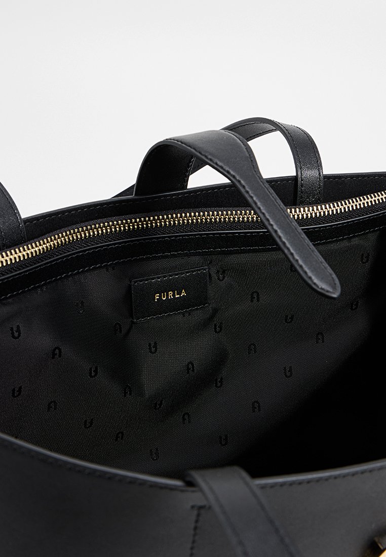 Intérieur d'un sac à main en cuir noir avec une texture lisse, une fermeture éclair dorée et une doublure en tissu arborant un motif logo subtil. Étiquette de marque visible.