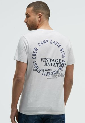 Helles graues Baumwoll-T-Shirt mit einem großen marineblauen Grafikdruck mit dem Text "Vintage Aviation" und zusätzlichen Details auf der Rückseite.