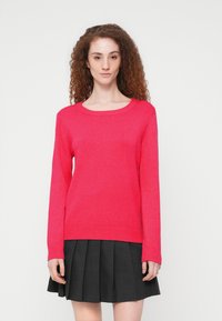 Φούξια πλεκτό πουλόβερ με στρογγυλή λαιμόκοψη και ριμπ μανσέτες, σε συνδυασμό με μαύρη φούστα με πιέτες. Λείο υλικό και απλός σχεδιασμός.