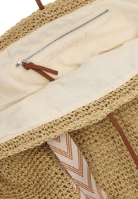 Geweven strooien tas met een beige voering, ritszak en bruine leren accenten. Voorzien van een gestreepte schouderband met perzik- en witte chevrons.
