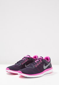 Scarpe da corsa Nike con tomaia in rete traspirante di un viola scuro, dettagli rosa e un' intersuola bianca. Il design include un logo ben visibile.