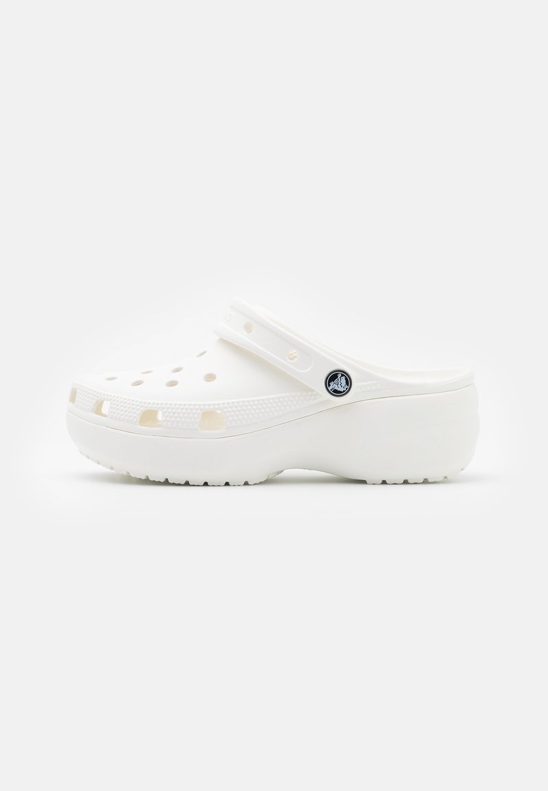 Sabot blanc à enfiler avec des trous de ventilation et une bride réglable, avec une semelle épaisse et un logo noir rond sur le côté.