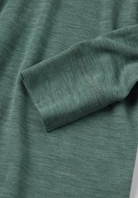 Vihreä neulekangas, jossa on yksityiskohtainen ompelu taitetussa hihansuussa, paljastaen tekstuurin ja saumanrakenteen.