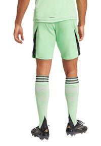 Grüne Sportshorts mit schwarzen seitlichen Akzenten, kombiniert mit hellgrünen Socken mit schwarzen und grauen Streifen sowie schwarzen Fußballschuhen.