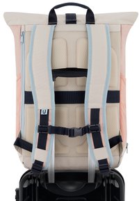 Mochila con correas acolchadas y hebilla en el pecho, sujeta al asa de un maleta negra con ruedas para facilitar su transporte durante el viaje.
