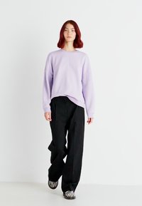 Svijetloplavi oversized dukserica, uparen s crnim širokim hlačama i cipelama sa zebrinim uzorkom u crno-bijeloj boji. Jednostavan dizajn, minimalistički stil.