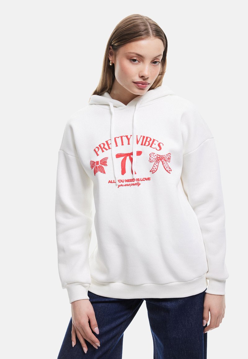 Biała bluza z kapturem wykonana z miękkiego materiału, z czerwonymi napisami graficznymi i wzorami kokardek z przodu. Projekt ma luźny krój i kieszeń kangurkę.