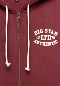 Felpa borgogna con zip e due lacci bianchi, con logo frontale crema: "BIG STAR 1979 LTD AUTHENTIC." Materiale testurizzato.
