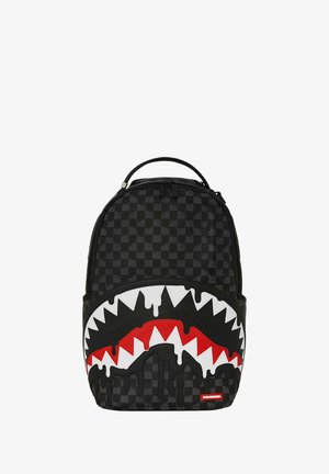 Mochila de cuadros negros con un diseño gráfico de boca de tiburón blanca y roja con bordes dentados, efecto de pintura negra que gotea y asa en la parte superior.