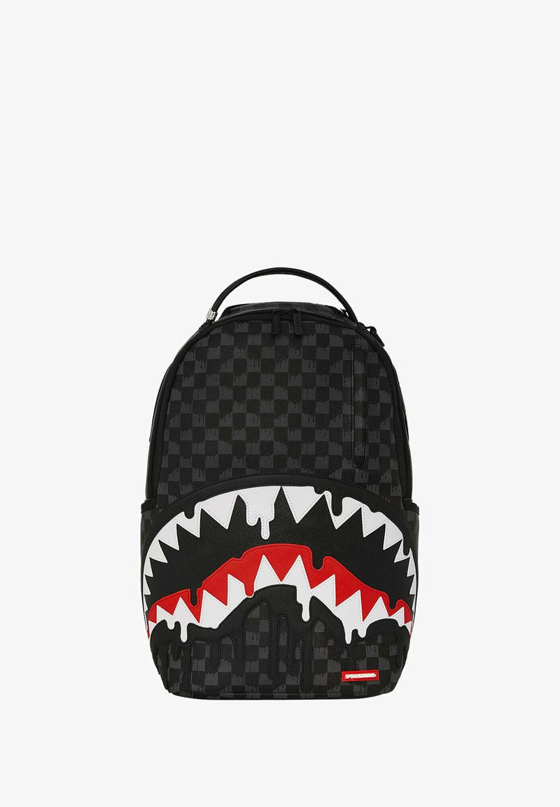 Mochila de cuadros negros con un diseño gráfico de boca de tiburón blanca y roja con bordes dentados, efecto de pintura negra que gotea y asa en la parte superior.