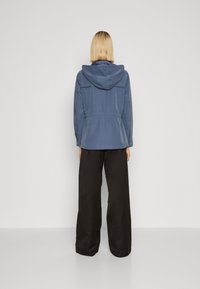 Blue, lightweight jacket with a hood, elastic waist, buttoned cuffs; paired with loose-fitting black pants. Smooth texture, casual design.