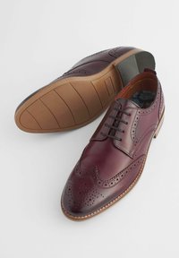 Brogues en cuir bordeaux avec une finition lisse, perforations décoratives, bout rond, laçage à cinq œillets et semelle en caoutchouc avec motif texturé.