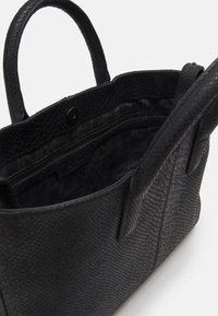 Svart texturerad läderhandväska med öppning längst upp, två handtag och en invändig ficka med dragkedja som har ett mönstrat foder.