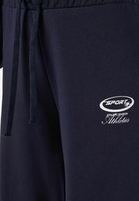 Jūras spēku treniņbikses, kas izgatavotas no mīksta auduma ar elastīgu jostu, ar auklu un baltu logotipu, kas lasāms "Sporta sportiskā nodaļa".