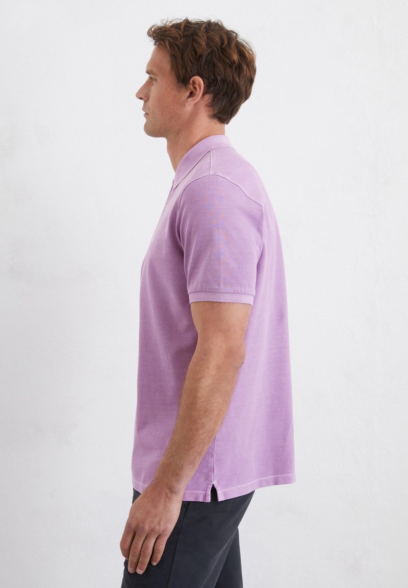 Fioletowa koszulka polo z krótkim rękawem, wykonana z lekkiego materiału, z klasycznym kołnierzykiem, bocznymi rozcięciami i luźnym krojem.