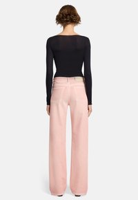 Jeans a gamba larga rosa pallido con vita alta, dotati di due tasche posteriori e dettagli di cucitura sottili, abbinati a un top fitted nero a maniche lunghe.