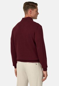 Bordeauxfarbener Strickpullover mit geripptem Kragen und Bündchen, im lässigen Schnitt und mit glatter Textur, kombiniert mit hellen Hosen.