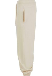 Jogging en beige en tissu doux, avec des poches latérales, une taille élastique et des poignets fuselés, conçus pour le confort et un usage facile.
