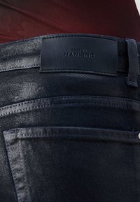 Tumed denim püksid, millel on nahast vöölabel "7 For All Mankind". Nähtavad õmblused ja klassikaline viie-tasku disain.