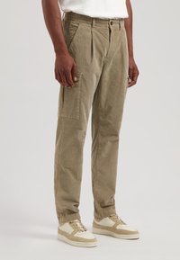 Kaki kordfløyelsbukser med rette ben, folder foran, sidelommer, og paired med beige sneakers.
