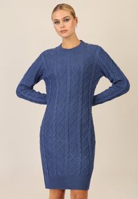 Abito in maglia a trecce di colore blu scuro. Presenta un collo rotondo, maniche lunghe e orlo a coste. Motivo a rombi testurizzati su tutta la superficie.