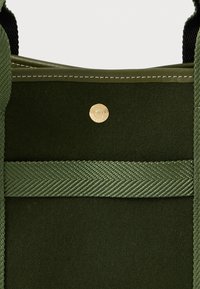 Borsa in suede verde scuro e tessuto con tracolla intrecciata verde oliva e un piccolo pulsante rotondo dorato sul pannello frontale.