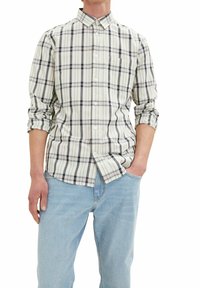Camisa de cuadros de algodón en crema, azul marino y burdeos, con cuello, mangas largas arremangadas y un bolsillo en el pecho. Jeans de color azul claro.