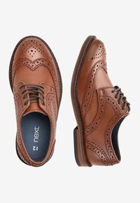 Brown leather brogue shoes featuring decorative perforations, laces, and a rounded toe. Sole is slightly raised with textured detail.