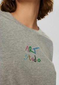 Šedé bavlnené tričko s farebným výšívaným textom "ART Studio". Klasický kruhový výstrih a mäkká, textúrovaná tkanina.