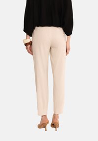 Beżowe, dopasowane spodnie o gładkiej fakturze i wąskim kroju, zestawione z brązowymi sandałami na wysokim obcasie, widok z tyłu.