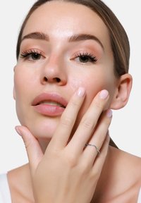 Srebrna pierścionek w kształcie fali na palcu modelki, o gładkiej fakturze; modelka ma delikatnie różowe paznokcie, naturalny makijaż i jasny odcień skóry.
