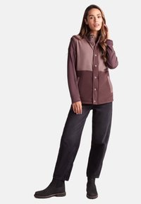 Fleece button-up jacket in shades of purple and brown, featuring a collar, front pockets, and a relaxed fit, paired with black pants and boots.