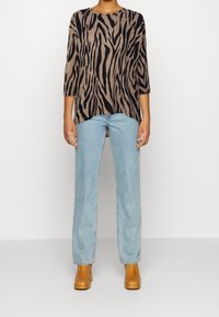 Brun och svart zebra-randig stickad topp med trekvartsärmar, kombinerad med ljusblå raka jeans och bruna stövlar.