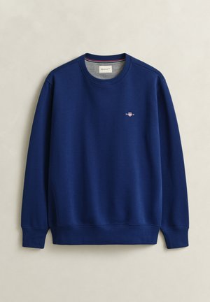 Sweat-shirt bleu marine à col rond avec poignets et ourlet côtelés, petit logo brodé sur le côté gauche de la poitrine, et doublure grise à l'intérieur du col.
