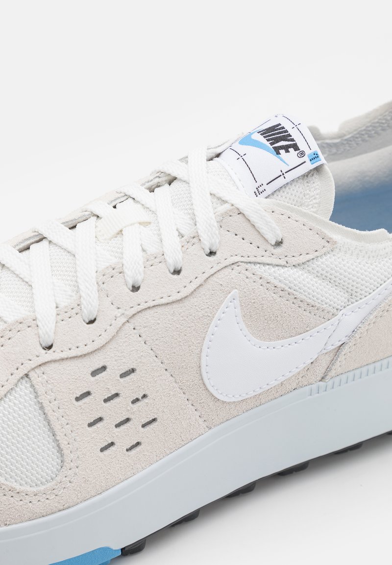 Zapatillas Nike con parte superior de ante y malla en beige claro, logo en blanco, acentos grises, cordones planos blancos y suela texturizada gris.
