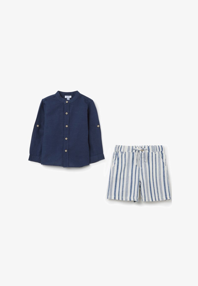 Camicia blu navy a maniche lunghe con bottoni e maniche arrotolabili; pantaloni corti a righe blu e bianche con vita elastica e tasche laterali.