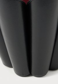 Čierna nádoba z umelého koženého materiálu s vlnitým dizajnom, má hladkú textúru a kontrastný červený vnútorný priestor.