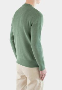 Grønn ribbestrikket genser med lange ermer, rund hals og tettsittende midje, kombinert med lyse beige bukser.